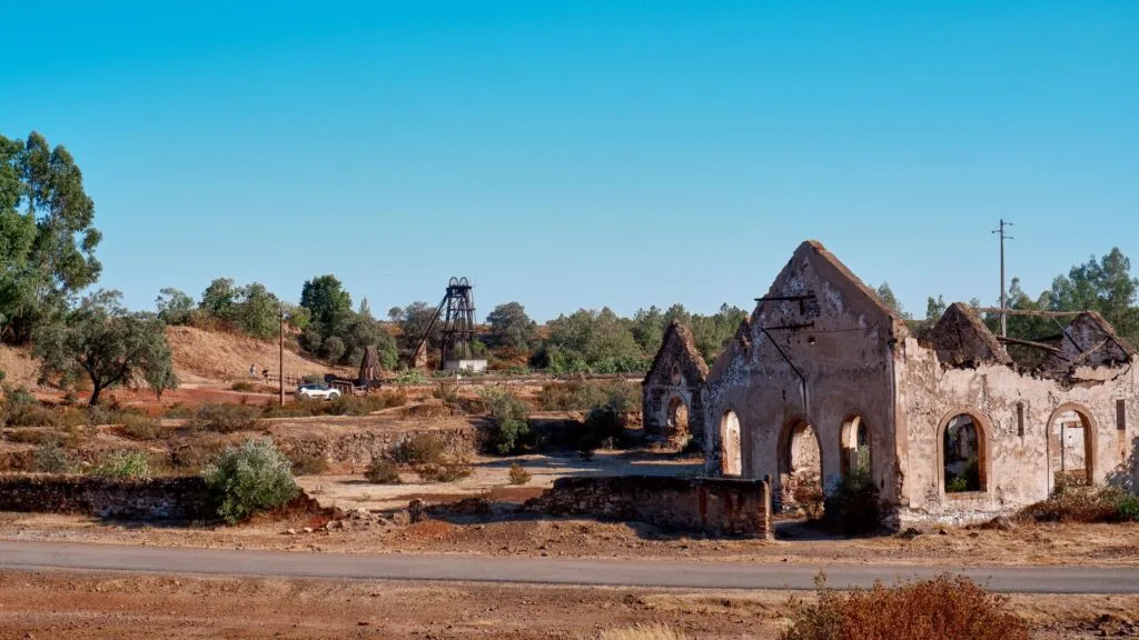 Ruderi di pietra con finestre ad arco in zona arida, con attrezzature minerarie sullo sfondo.