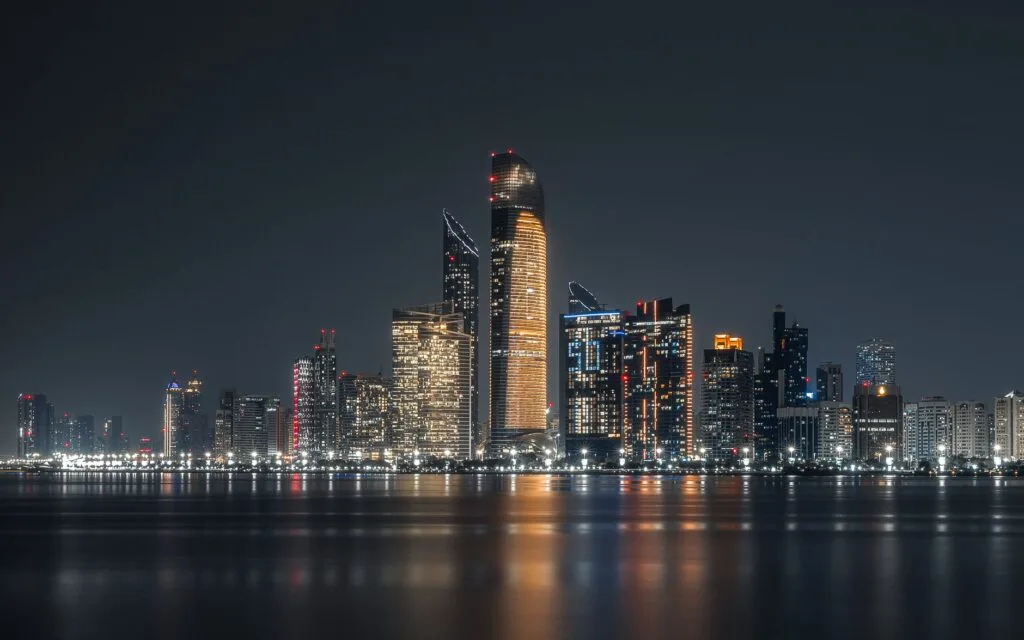 Skyline notturna di Abu Dhabi con grattacieli illuminati riflessi nelle acque del golfo.