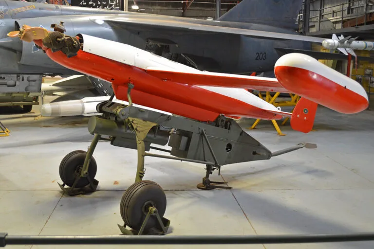 Drone tattico rosso e bianco con carrello di lancio a terra in un hangar, corpo affusolato e ali a delta caratteristiche.