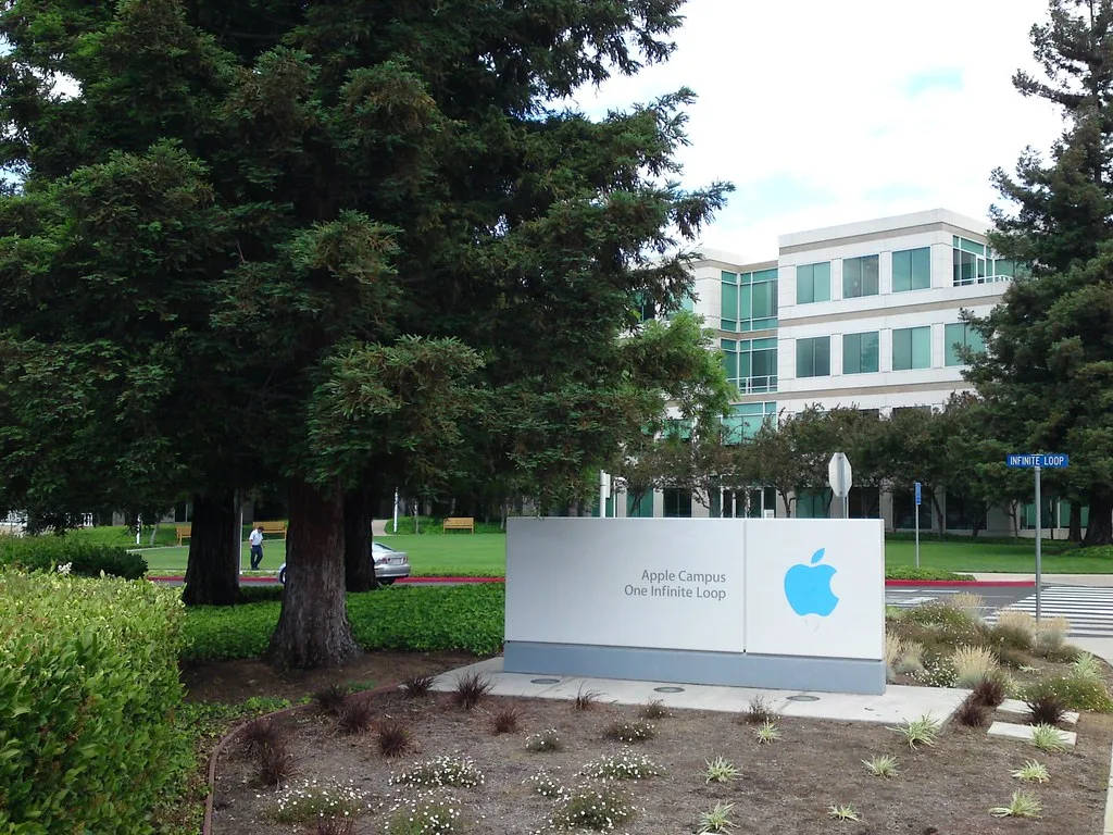 Insegna del campus Apple con il logo della mela davanti a un edificio moderno circondato da alberi.