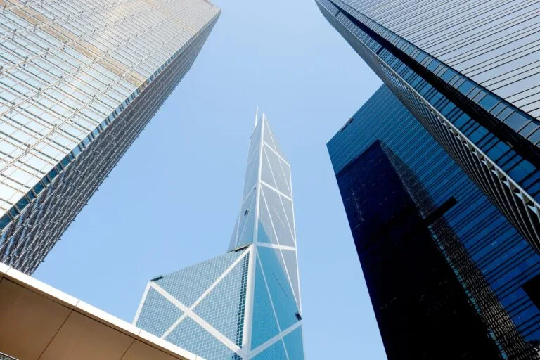 Grattacieli moderni fotografati dal basso verso l'alto, con forme geometriche in vetro e acciaio contro cielo azzurro.