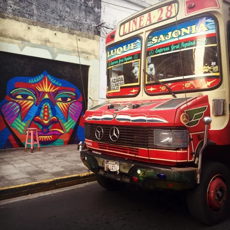 Autobus rosso e beige parcheggiato davanti a un murale colorato con volto stilizzato blu, rosso e giallo.
