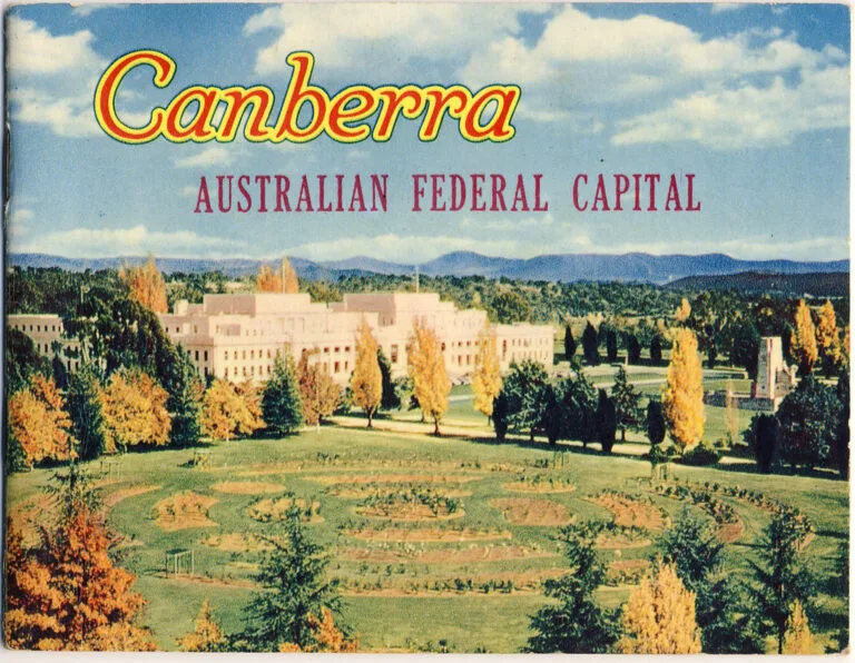 Palazzo del Parlamento australiano circondato da alberi in autunno e colline boscose sullo sfondo.