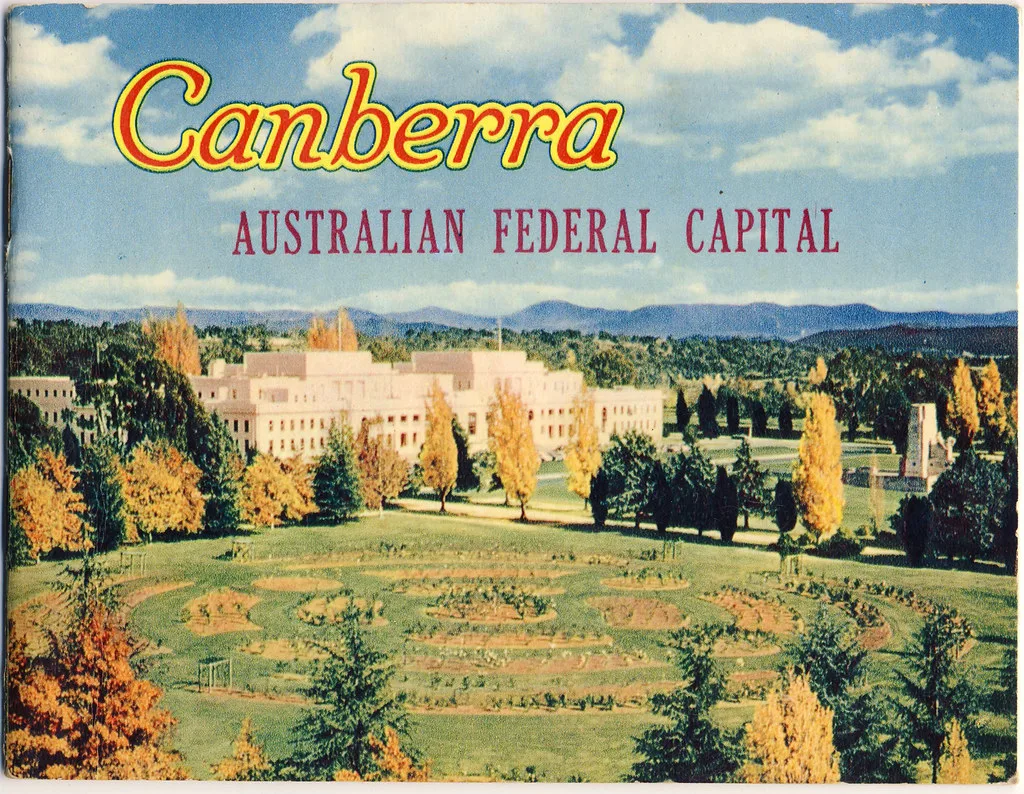 Palazzo del Parlamento australiano circondato da alberi in autunno e colline boscose sullo sfondo.