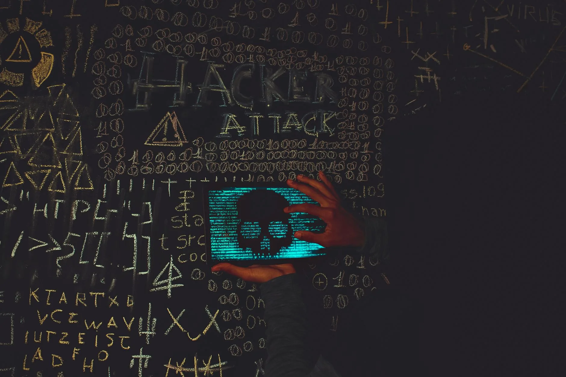 Mano su tablet che mostra un teschio blu circondato da simboli di codice e scritta 'Hacker Attack' su fondo scuro.