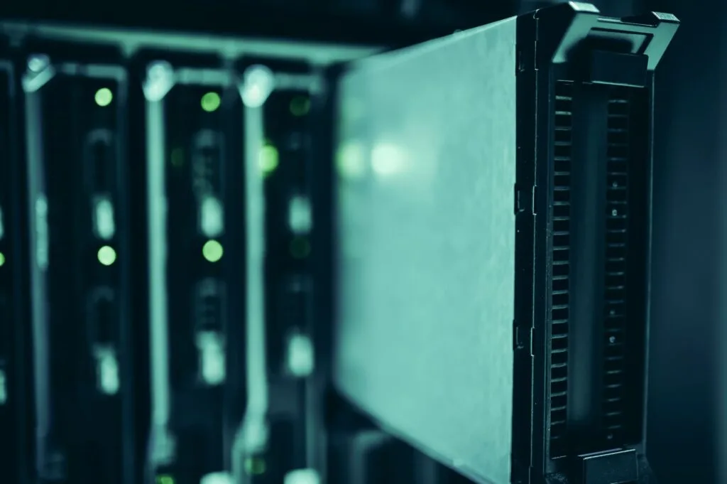Server in rack con spie luminose verdi accese in una sala dati, illuminati da luce blu-verde.