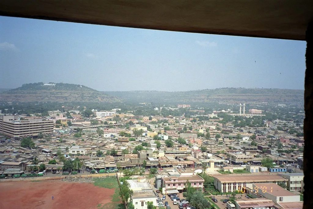 Panorama di Bamako con edifici residenziali e commerciali circondati da colline verdi sullo sfondo.