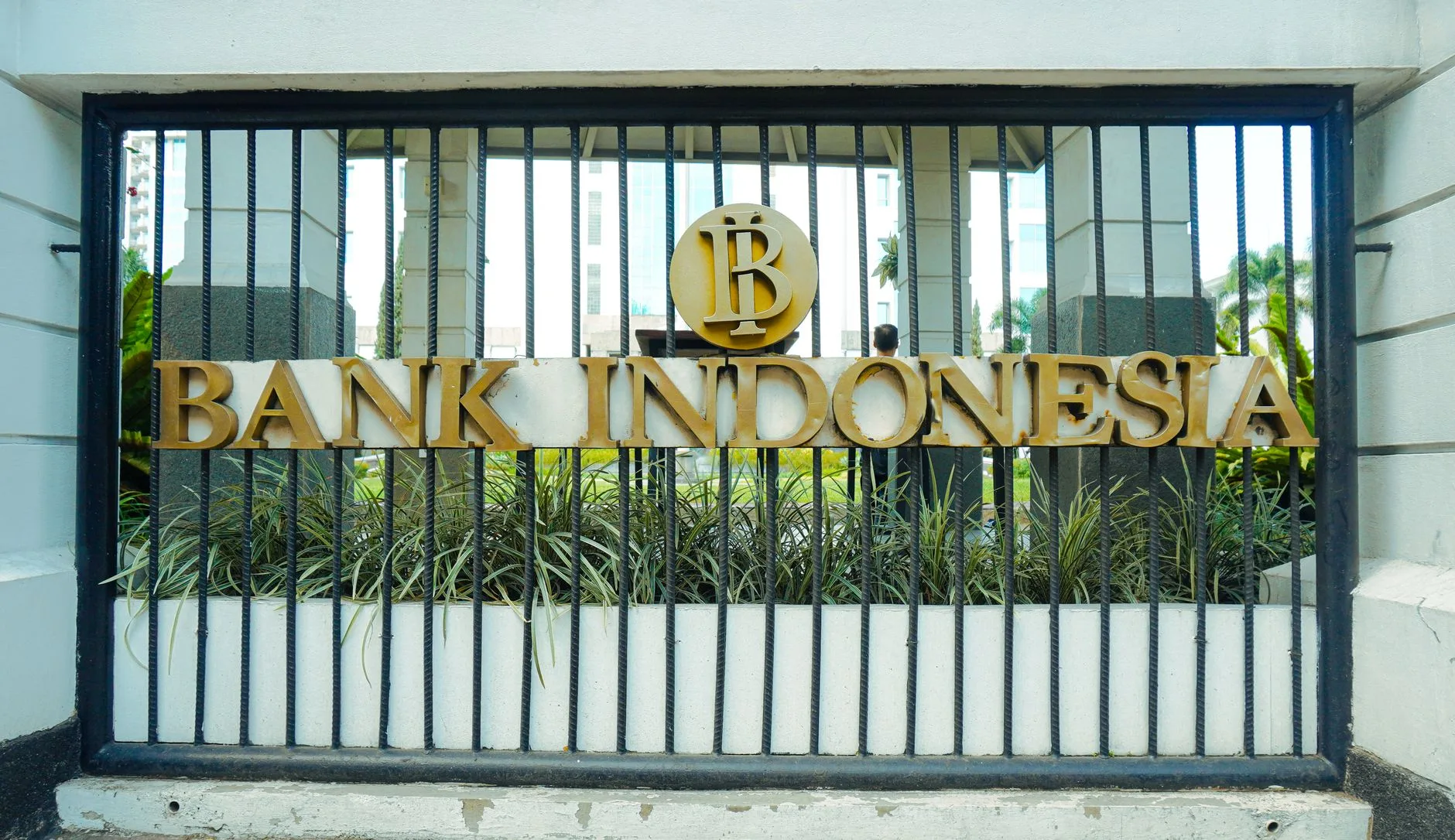 Cancellata d'ingresso della Bank Indonesia con logo dorato e scritta metallica, edificio vetrato sullo sfondo.