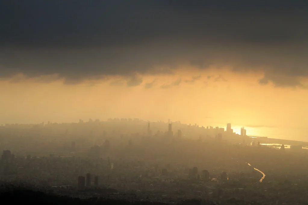 Skyline di una città avvolta nella nebbia e smog, con il sole che filtra attraverso la foschia.