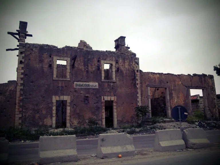 Edificio in rovina con muri sgretolati, finestre vuote e una croce in cima, circondato da blocchi di cemento.