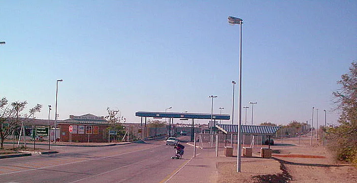 Stazione di autobus con strutture moderne e pali dell'illuminazione in un'area urbana semivuota sotto cielo sereno.