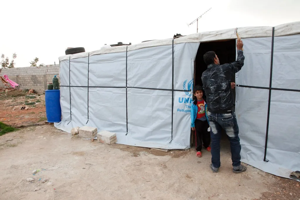 Uomo entra in una tenda bianca con logo UNHCR in un campo profughi in Libano orientale.