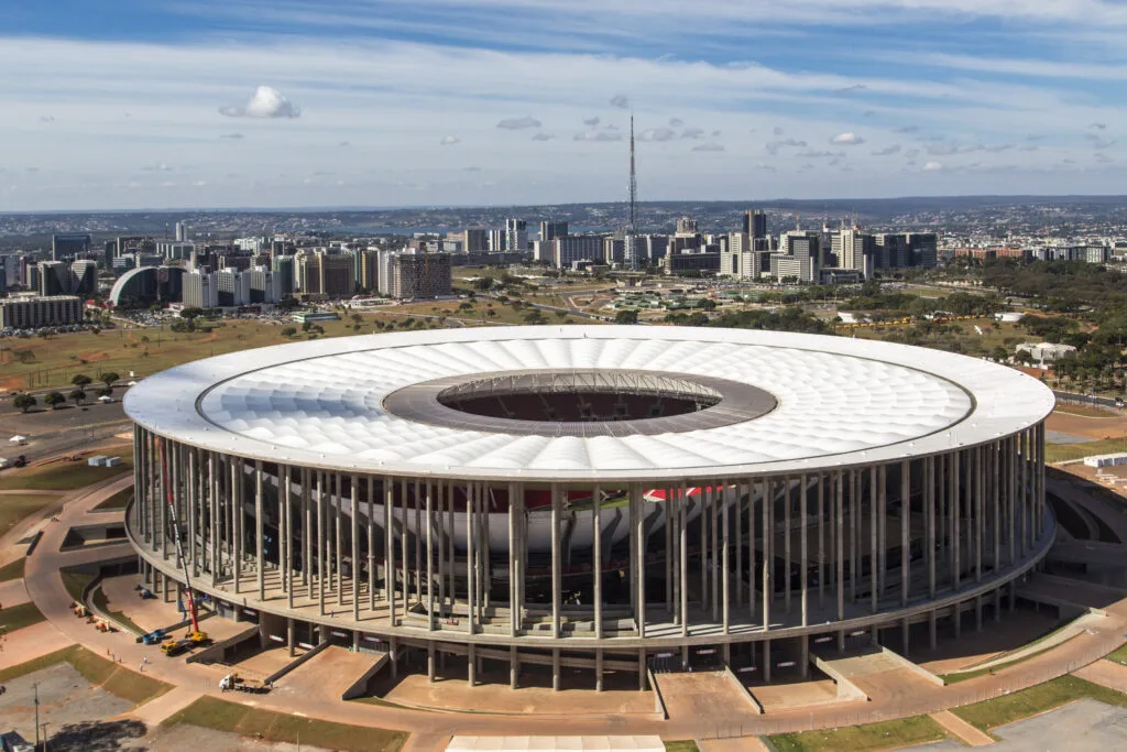 Stadio nazionale di Brasilia con copertura circolare bianca, visto dall'alto con la capitale sullo sfondo.