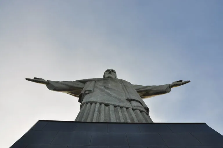 Il Cristo Redentore di Rio de Janeiro con le braccia tese, inquadrato dal basso contro il cielo nuvoloso.
