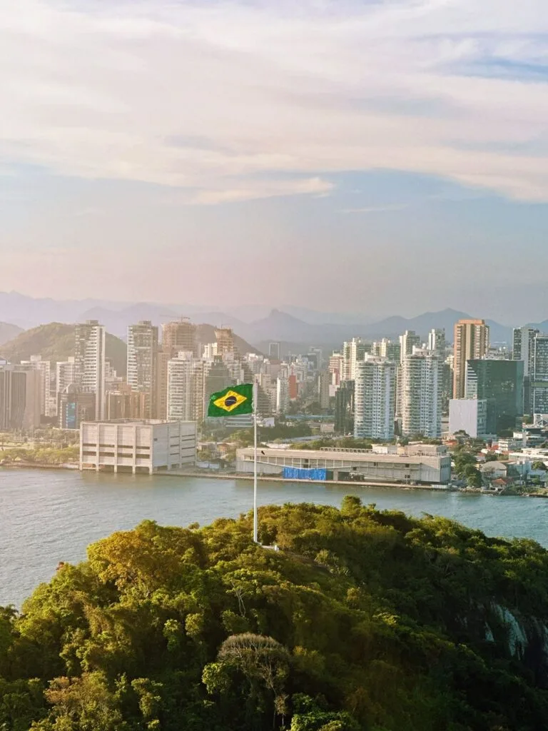 Bandiera brasiliana sventola su una collina verdeggiante con la città e la baia sullo sfondo.
