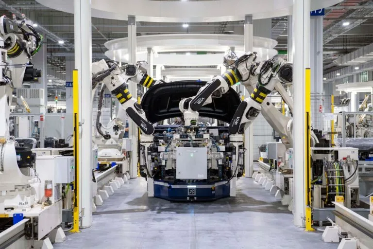 Bracci robotici con strisce gialle e nere assemblano un motore auto in linea di produzione automatizzata.