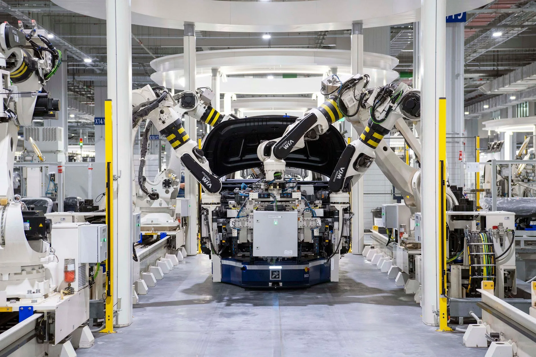 Bracci robotici con strisce gialle e nere assemblano un motore auto in linea di produzione automatizzata.