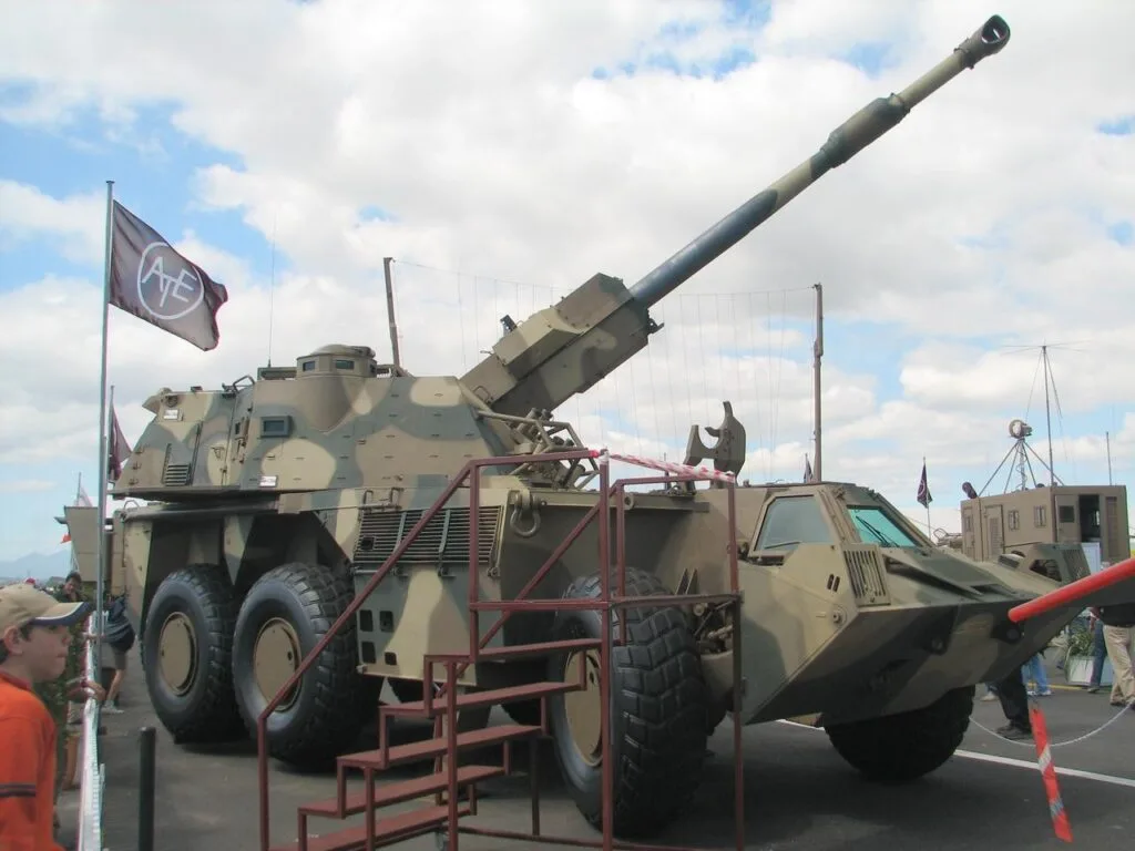 Veicolo blindato tattico con torretta armata e bandiera sudafricana esposto in una base militare.