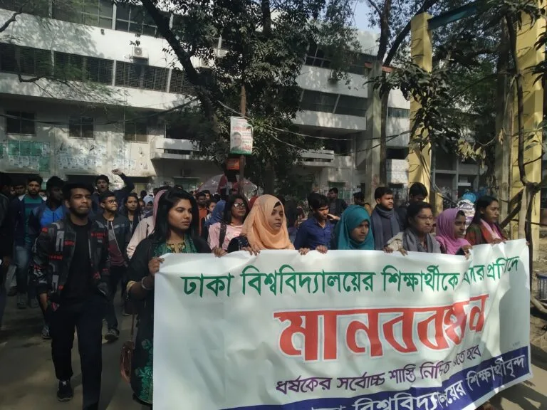 Studenti bangladesi manifestano in strada con striscioni in bengali davanti a edifici universitari.