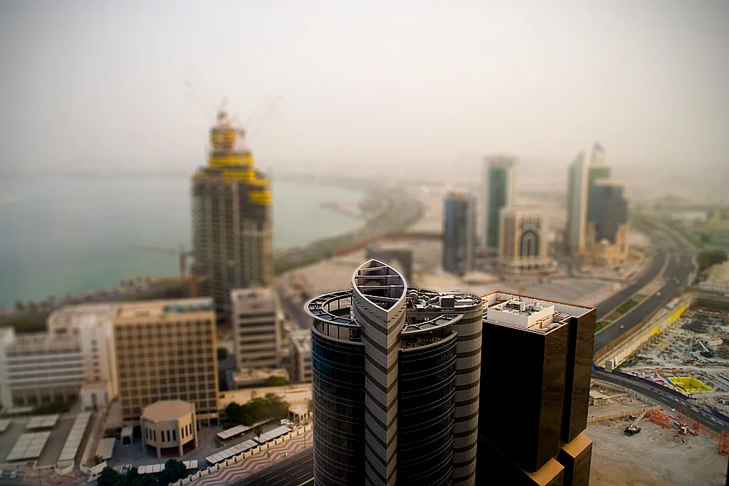 Skyline di Doha con grattacieli moderni in primo piano e la baia del Golfo Persico sullo sfondo nella foschia.