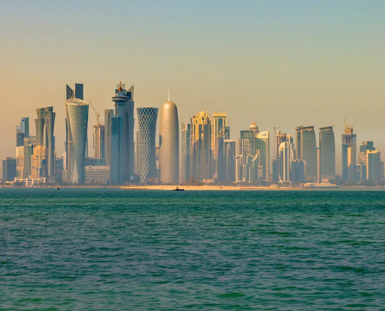 Lo skyline di Doha al tramonto con grattacieli moderni e dalle forme geometriche affacciati sulla baia turchese.