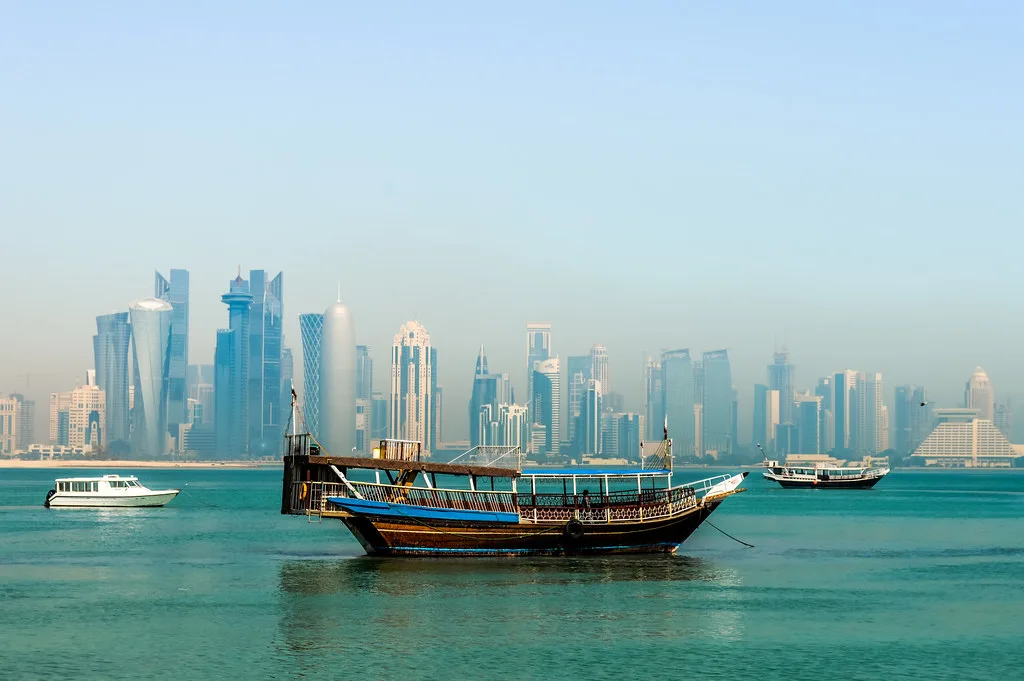 Tradizionale dhow in legno ancorato nelle acque turchesi davanti allo skyline di grattacieli moderni di Doha.
