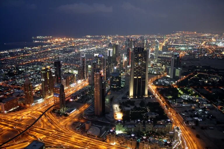 Metropoli del Golfo illuminata di notte con grattacieli, svincoli stradali e espansione urbana che si estende all'orizzonte.