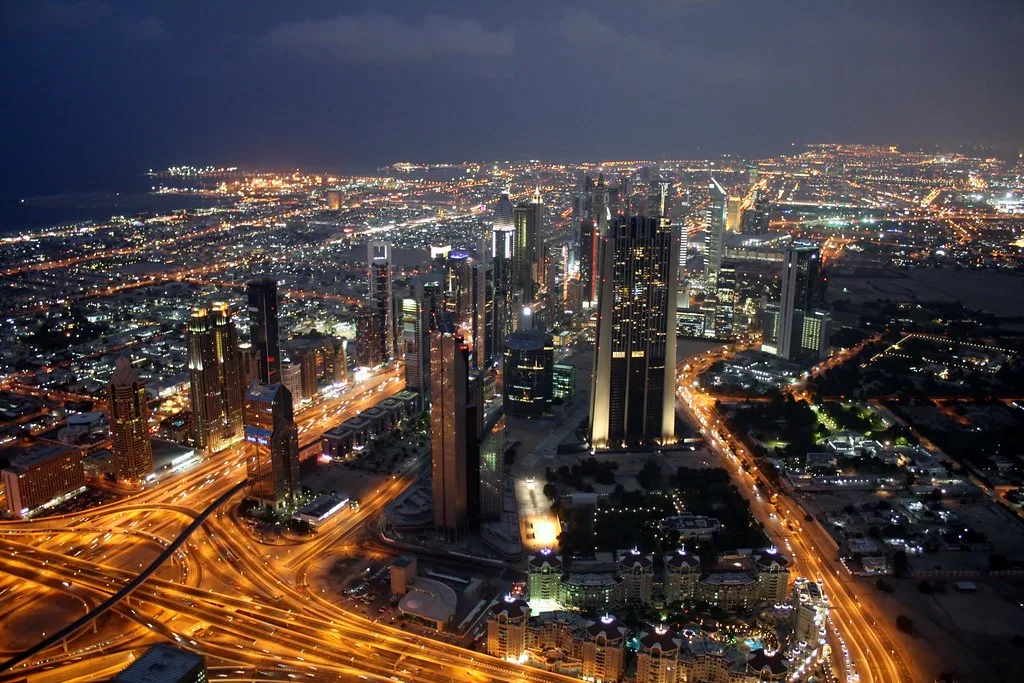 Metropoli del Golfo illuminata di notte con grattacieli, svincoli stradali e espansione urbana che si estende all'orizzonte.