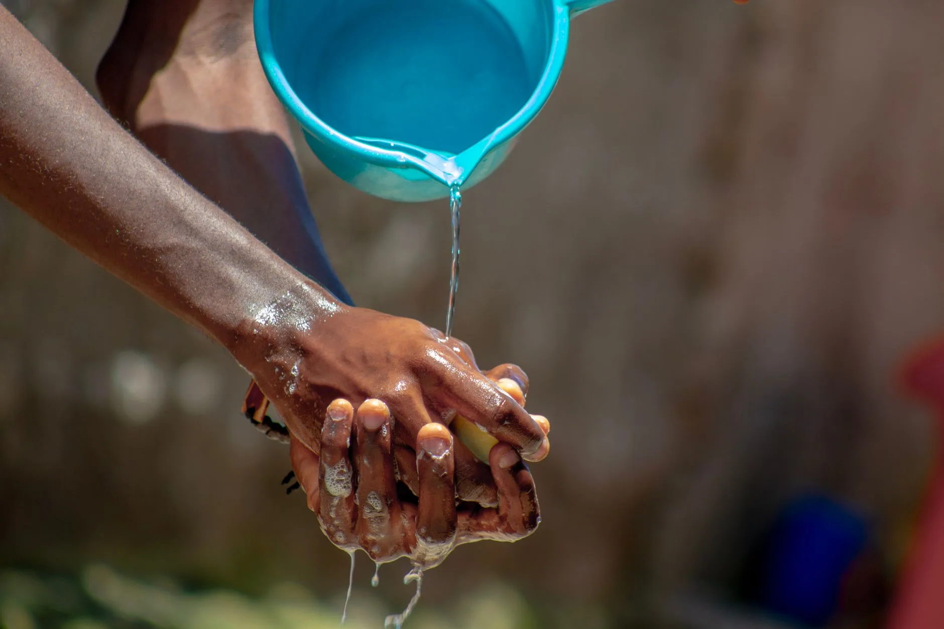 Una mano bagnata da acqua versata da un secchio blu durante un'operazione di igiene.