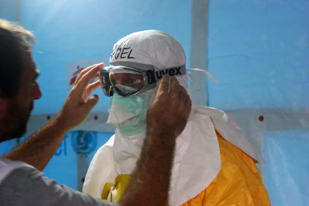Operatore sanitario indossa dispositivi di protezione individuale e occhiali in una struttura medica.