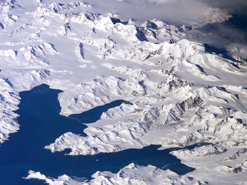 Catena montuosa innevata affacciata su acque blu scuro, fotografata dall'alto in una veduta aerea.