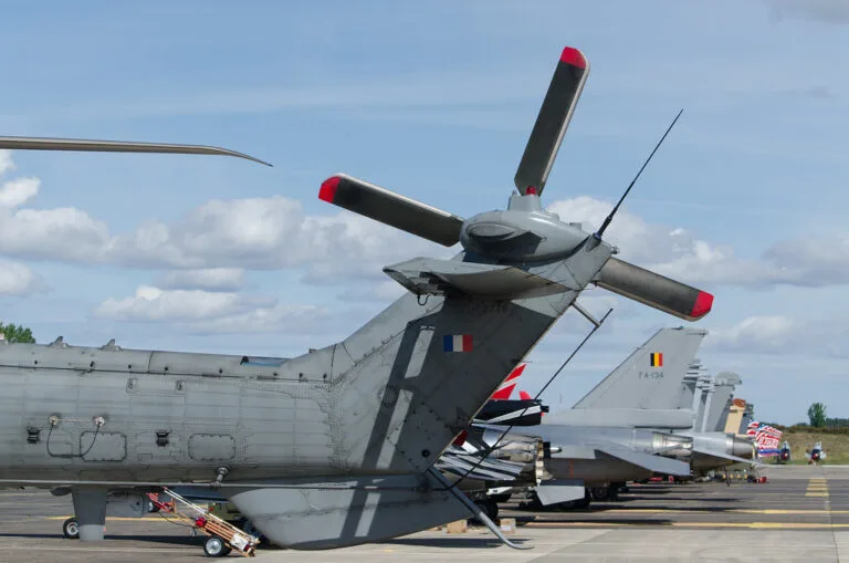 Coda di un aereo militare da trasporto con bandiera francese e motori a elica con coprimozzo rossi in una base aerea.