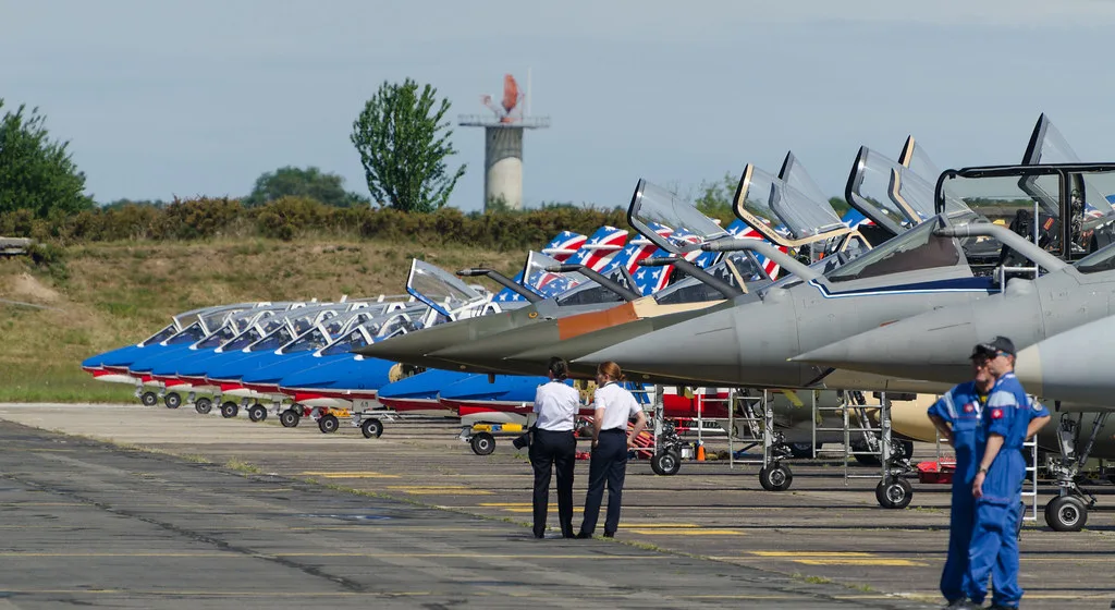 Aereo da combattimento con livrea blu e bandiera francese in area operativa, circondato da personale.