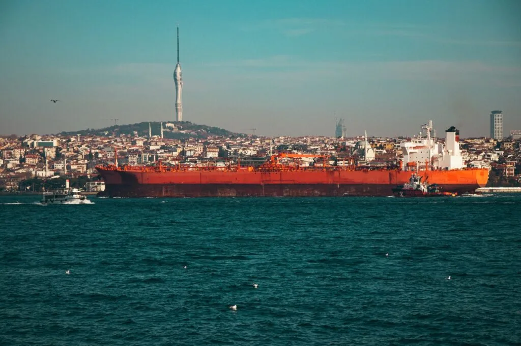 Una grande petroliera rossa naviga nello Stretto del Bosforo con lo skyline di Istanbul e la Torre Camlica sullo sfondo.
