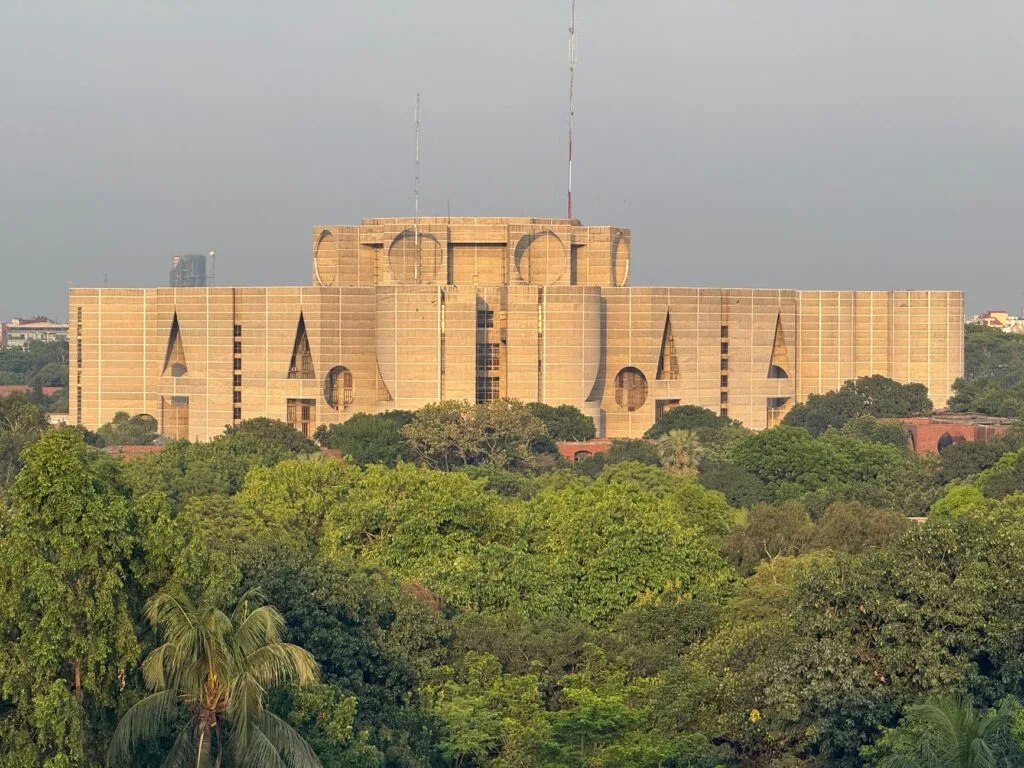 Edificio parlamentare con architettura monumentale in mattoni gialli circondato da vegetazione rigogliosa.