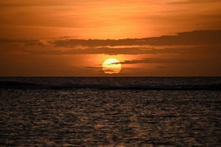 Sole al tramonto tocca l'orizzonte dell'Oceano Indiano con cielo arancione e mare calmo.