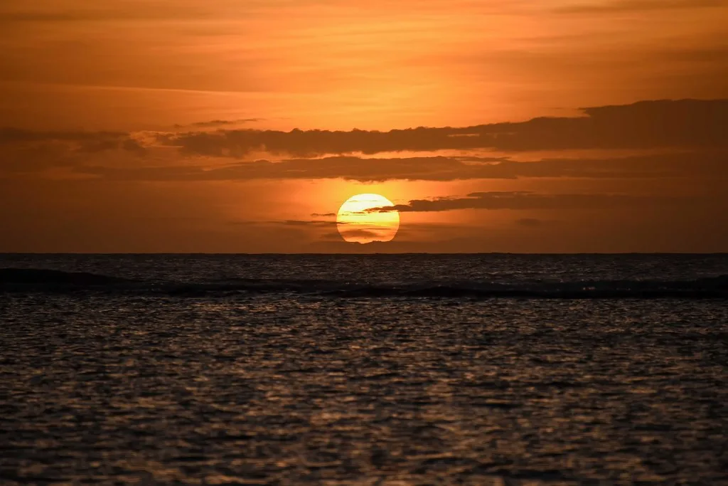 Sole al tramonto tocca l'orizzonte dell'Oceano Indiano con cielo arancione e mare calmo.