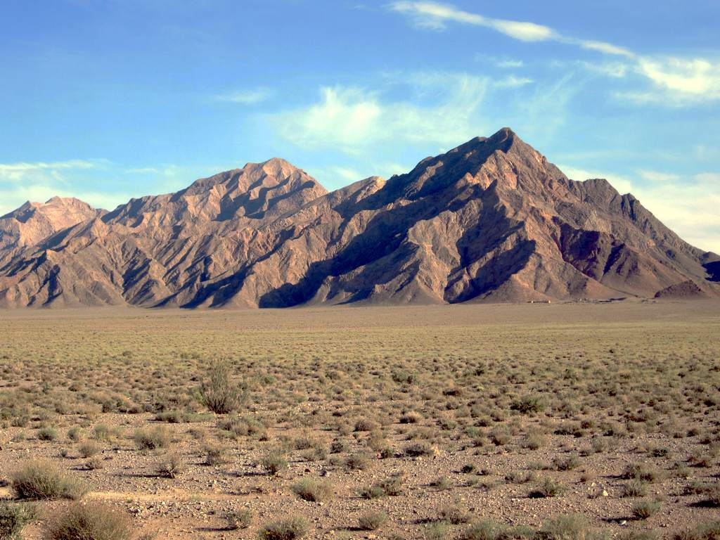 Catena montuosa aspra e rocciosa che sorge da un altopiano desertico semiarido con vegetazione rada.