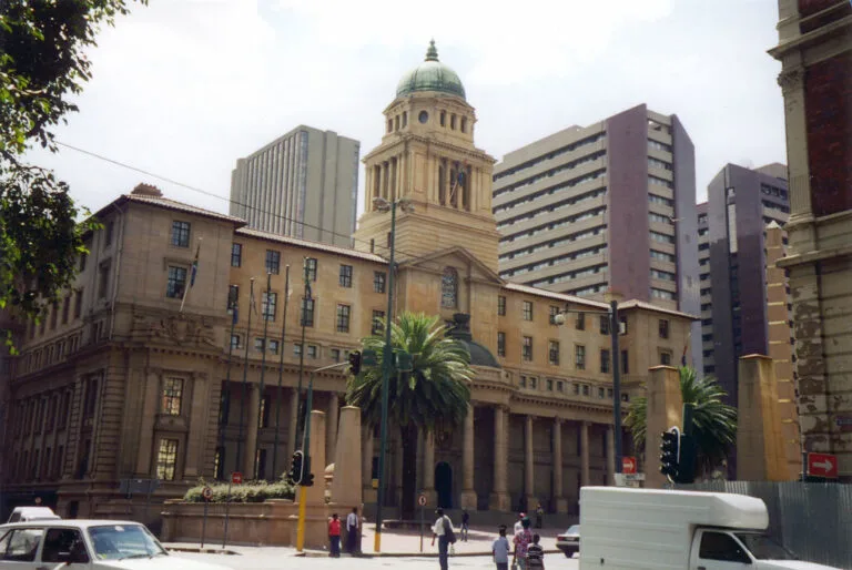 La City Hall di Johannesburg con la sua cupola verde circondata da edifici moderni e palme, in una piazza cittadina.