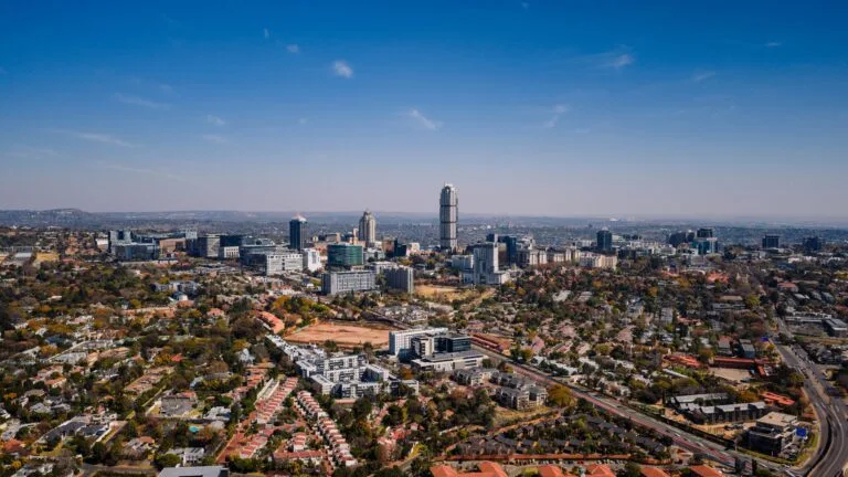 Veduta aerea di Johannesburg con grattacieli circondati da aree residenziali sotto cielo sereno.