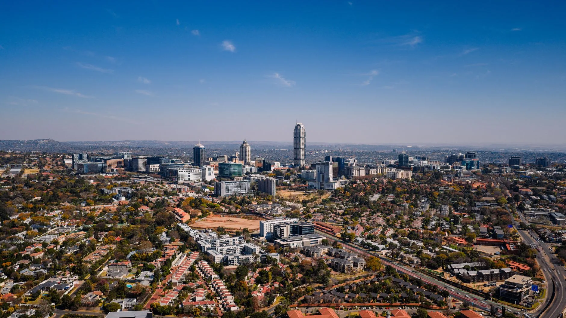 Veduta aerea di Johannesburg con grattacieli circondati da aree residenziali sotto cielo sereno.