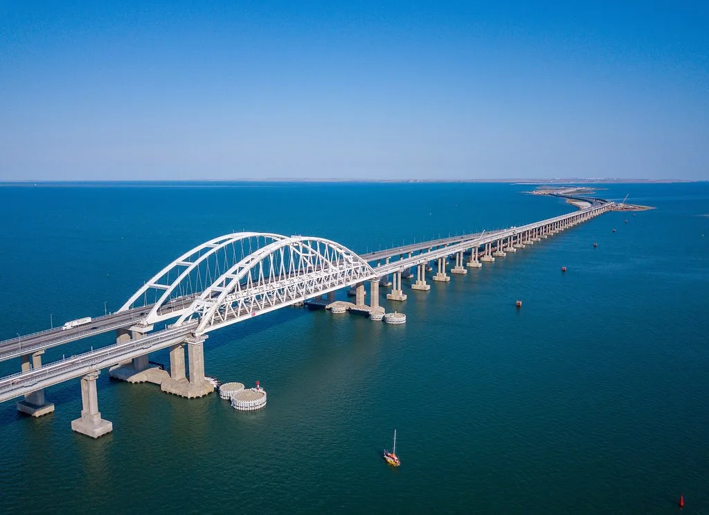 Ponte ad arco bianco attraversa acque azzurre con piloni di cemento, collegando due sponde con struttura rettilinea.