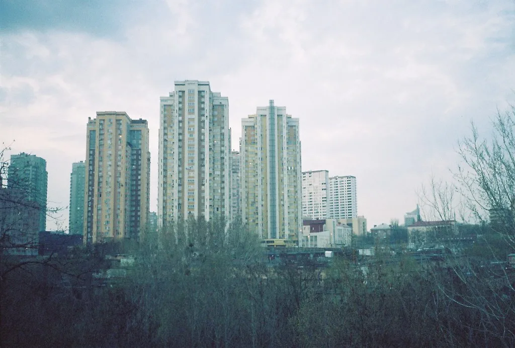 Palazzi residenziali di diversi piani in un paesaggio urbano con alberi spogli in primo piano e cielo nuvoloso.