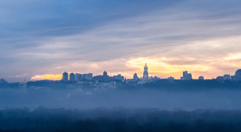 Lo skyline di una città con grattacieli illuminati all'alba emerge dalla nebbia fitta che copre il territorio circostante.