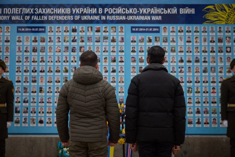 Due persone osservano un muro commemorativo con fotografie di caduti della guerra russo-ucraina.