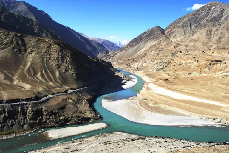 Due fiumi ad acque di colore diverso confluiscono in una valle himalayiana tra montagne aride e rocciose.