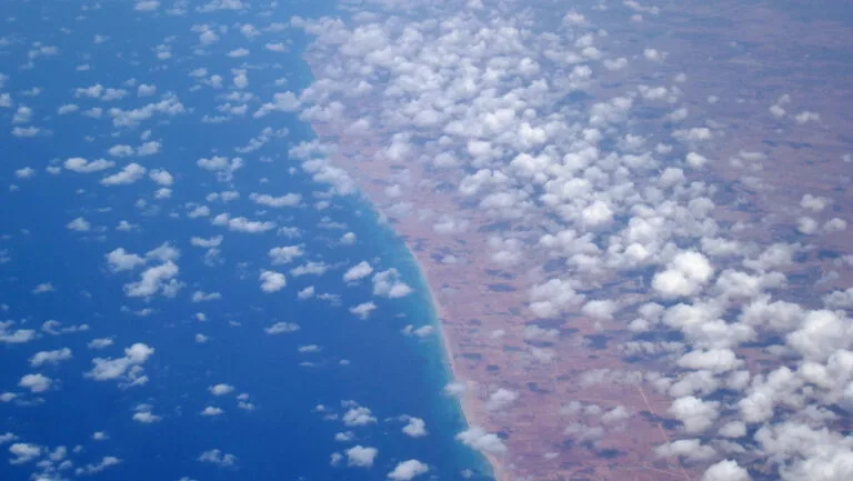 Veduta aerea con oceano blu a sinistra e costa desertica sabbiosa a destra, separati da una linea costiera netta.