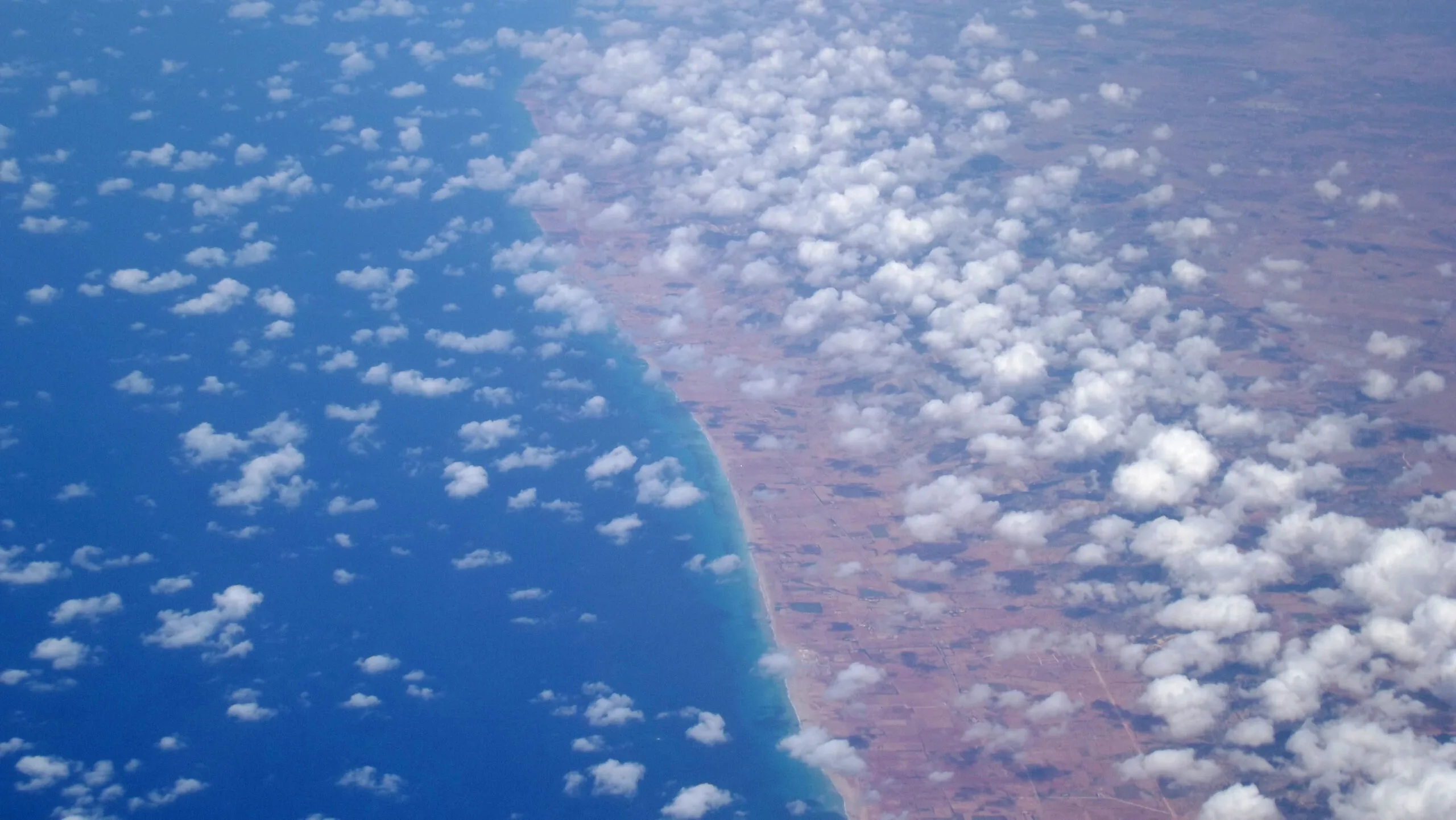 Veduta aerea con oceano blu a sinistra e costa desertica sabbiosa a destra, separati da una linea costiera netta.