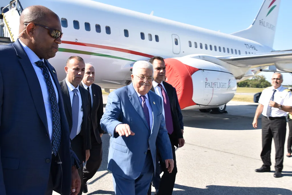 Delegazione palestinese scende da aereo con bandiera nazionale sulla fusoliera in giornata soleggiata.