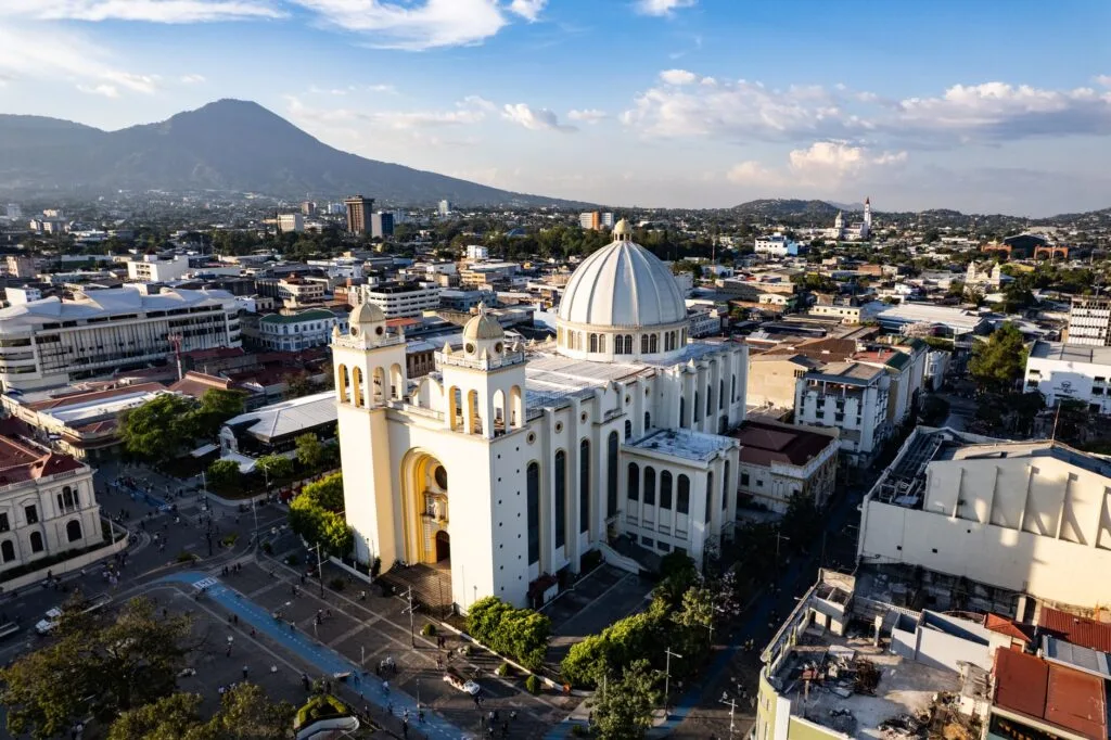 Cattedrale bianca con cupola dorata in primo piano domina il panorama urbano, con vulcano sullo sfondo.